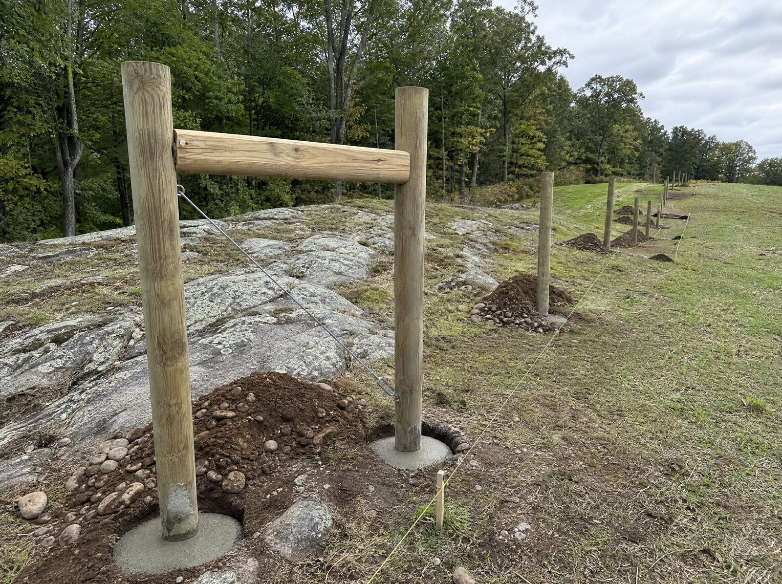 Wood fence posts and an H-brace corner and end assembly being set in rocky New Fairfield ground with no wire strung yet on a tidy site