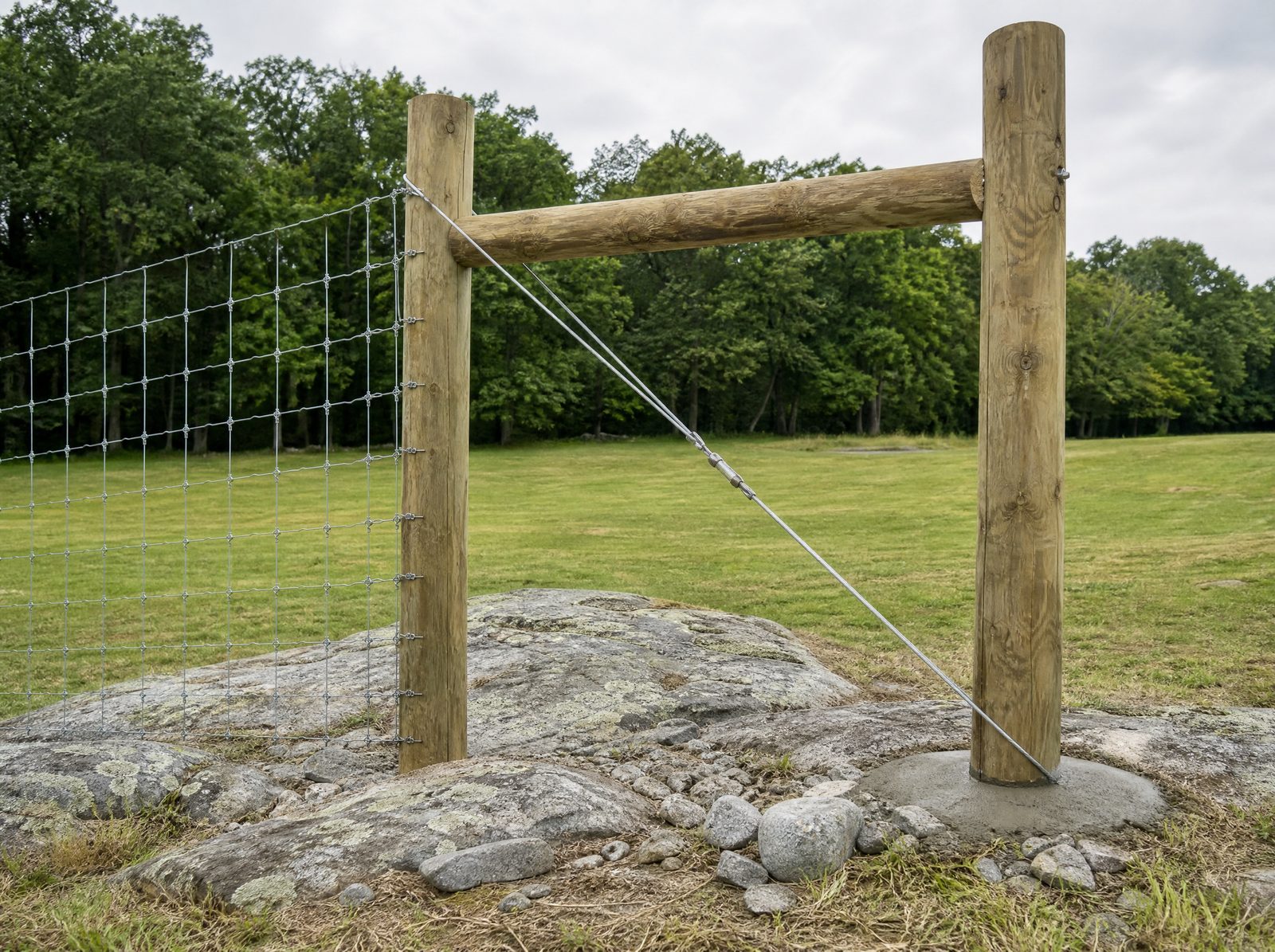Wood H-brace corner assembly with a diagonal tension wire set into rocky Southbury ground at the end of a woven wire run, carrying the wire tension