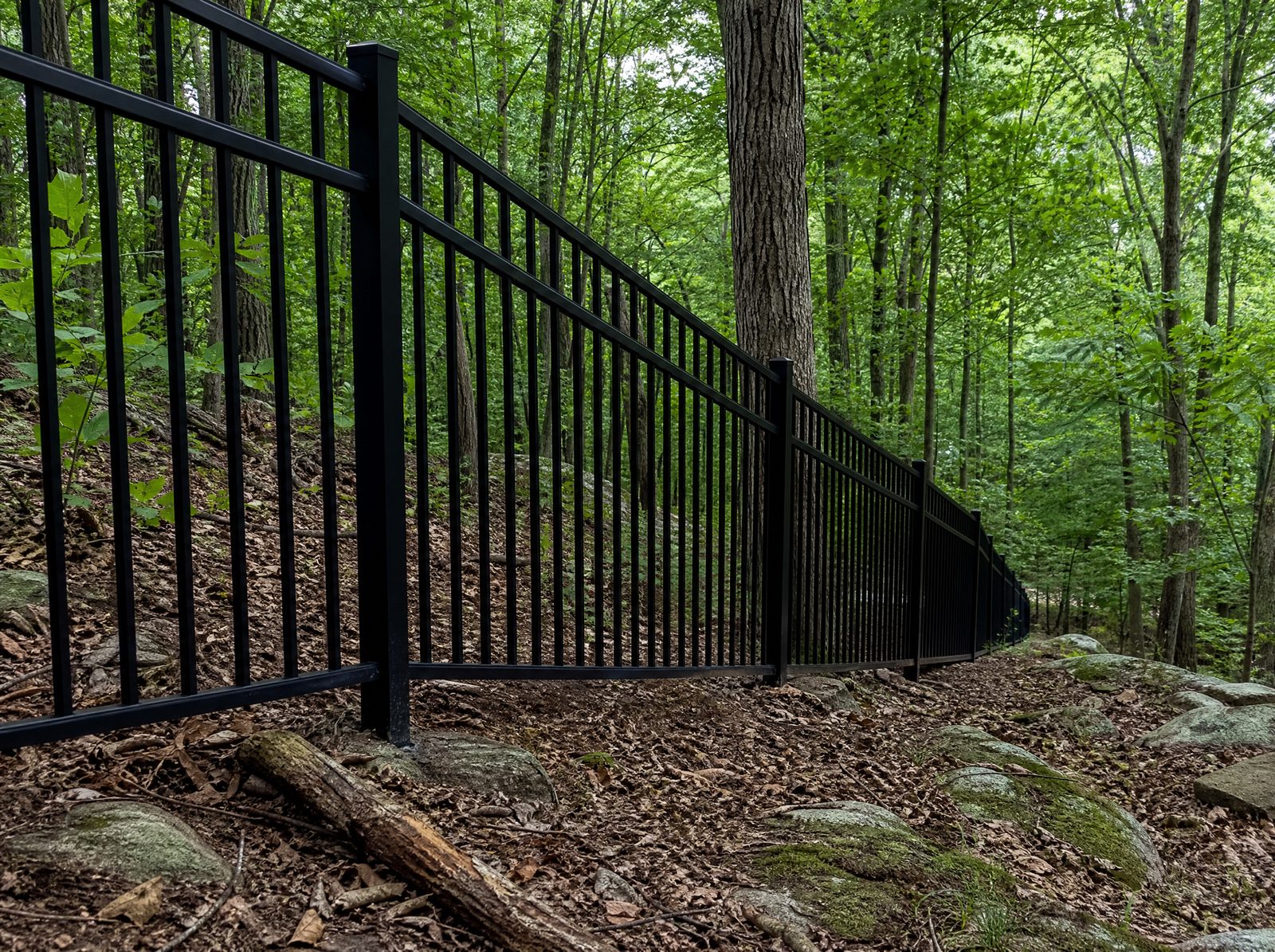Rackable black aluminum fence following a downhill grade in a continuous line along a wooded property boundary