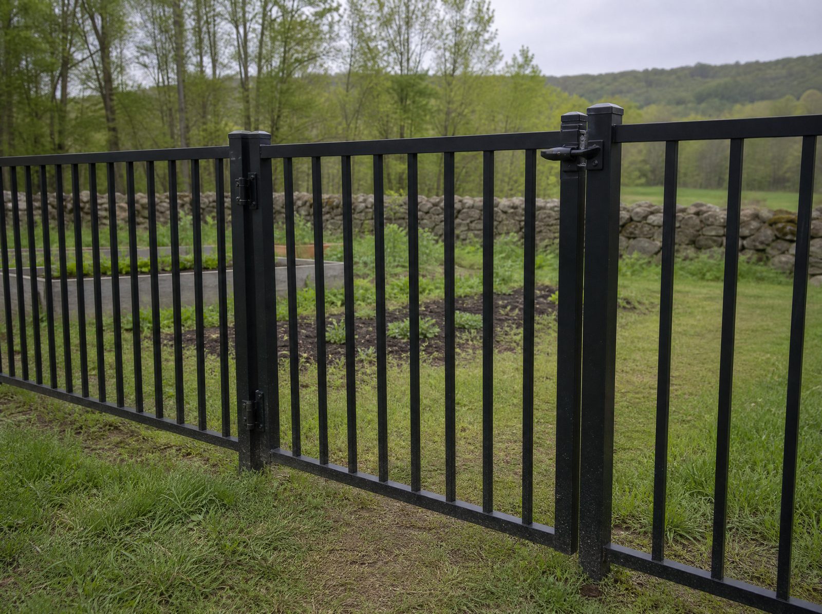 Black aluminum self-closing walk gate with self-latching hardware set into a continuous four foot flat-top aluminum fence run at a farmhouse kitchen garden