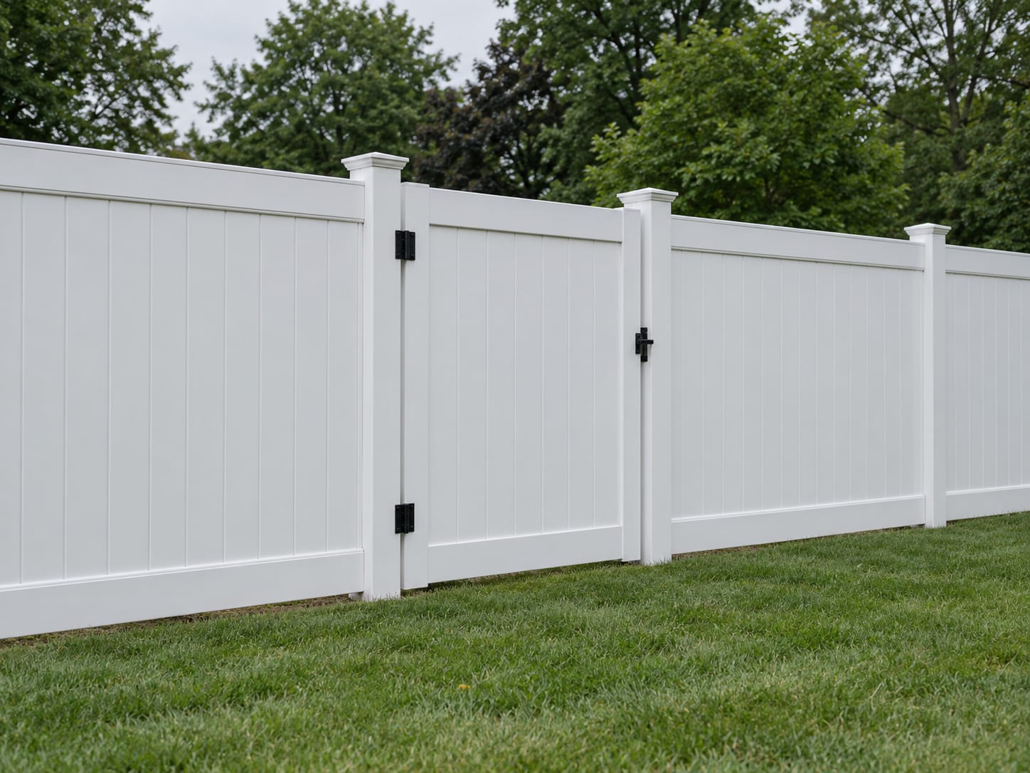 A tall white vinyl privacy fence with a closed gate stands on level ground in a western Connecticut backyard.