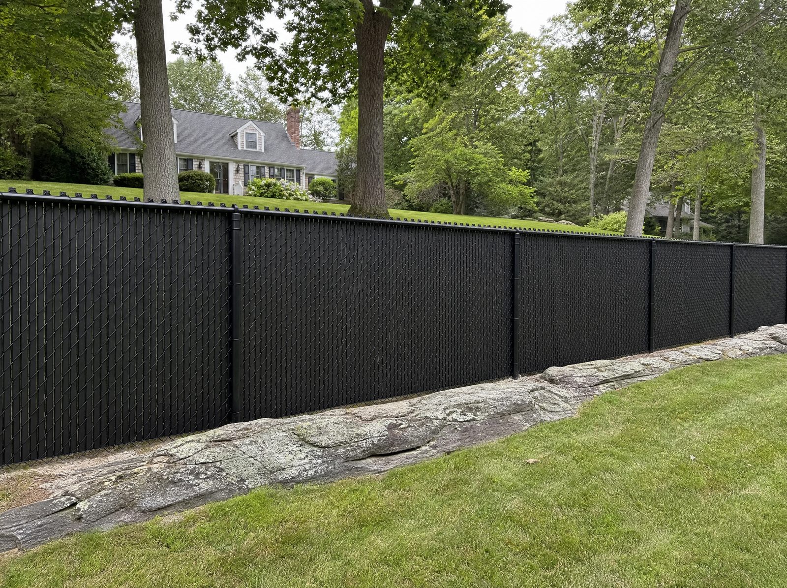 Five foot black polymer-coated chain-link fence with vertical privacy slats woven through the mesh along a New Fairfield residential property boundary