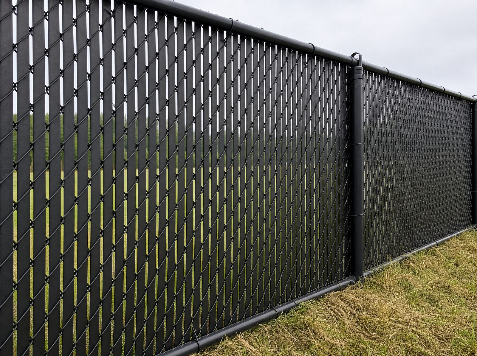 Five to six foot black chain link fence with vertical black privacy slats woven through the diamond mesh screening the run on a rural Southbury property