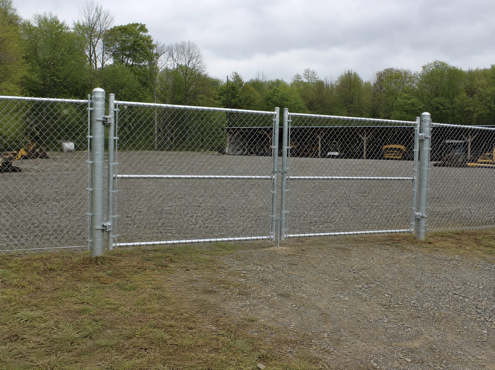 Six foot commercial galvanized chain-link fence with a closed double swing vehicle gate securing a gravel service and equipment yard at a Southbury business property