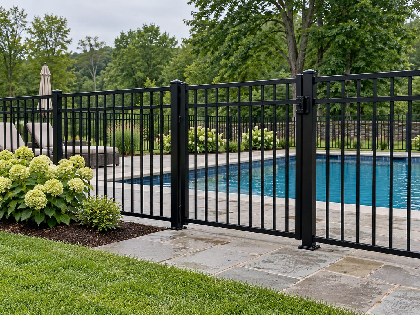 A black aluminum pool fence with a closed self-latching gate encloses an in-ground pool and its deck beside a lawn in western Connecticut.
