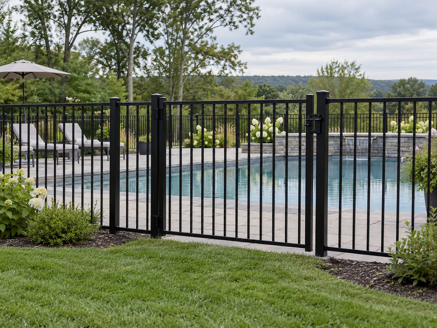 A black aluminum fence with a closed self-latching gate enclosing a backyard pool deck in a western Connecticut neighborhood.