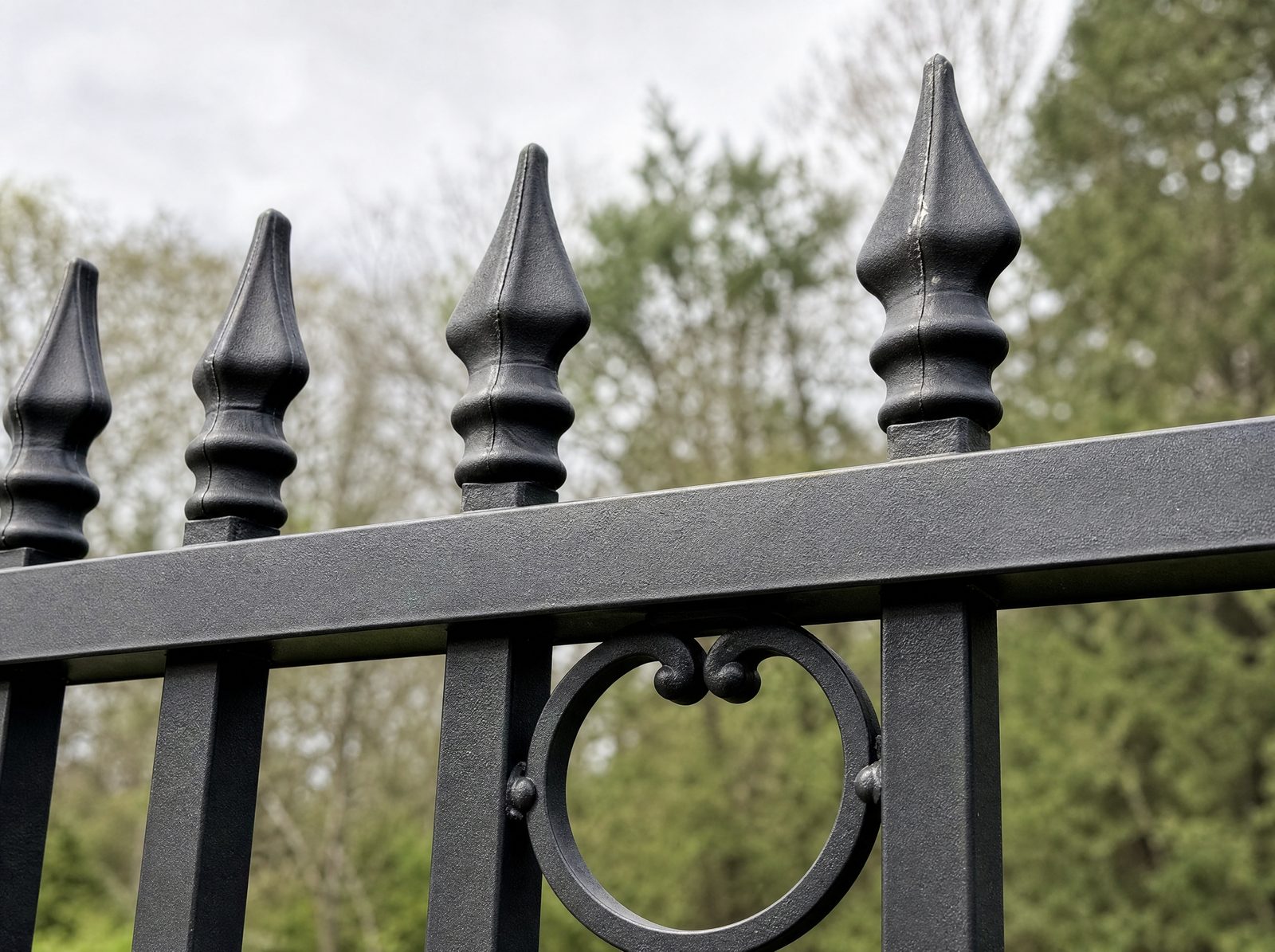 Close view of black cast finials on top of ornamental pickets and a decorative scroll ring casting set into the top rail