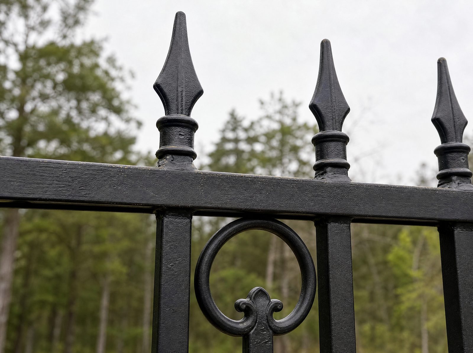 Close view of black cast finials on top of ornamental pickets with a decorative scroll ring casting set into the top rail