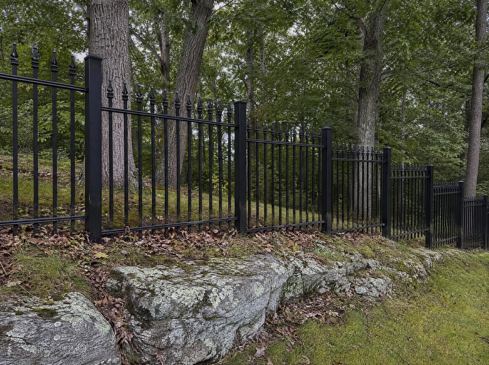 Four foot black ornamental metal fence with cast finials stepping down a sloped ledge-heavy Sherman yard in level panels