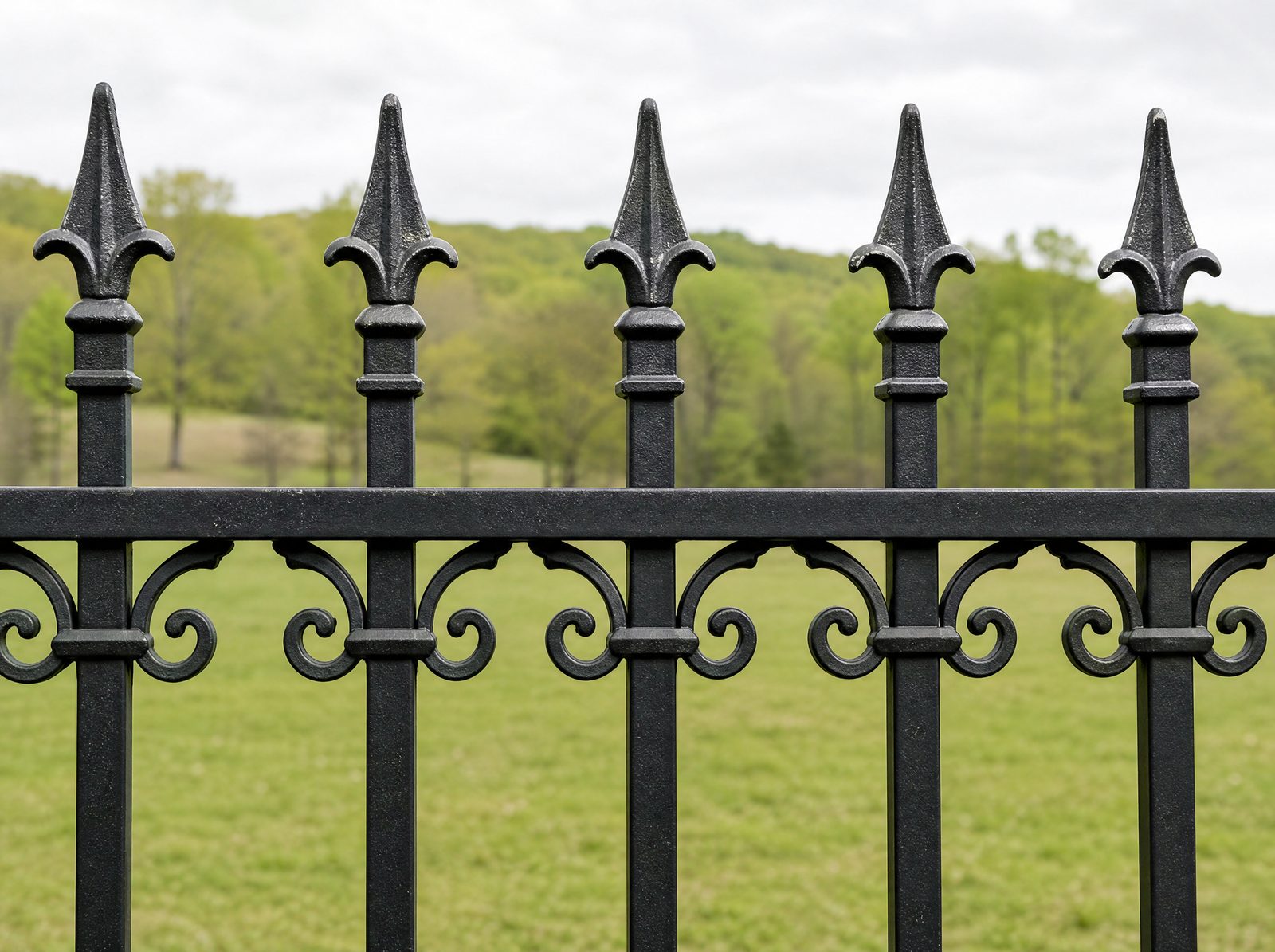 Close honest shot of the top of a black ornamental fence showing cast spear-top finials and a decorative scroll or ring casting worked below the top rail