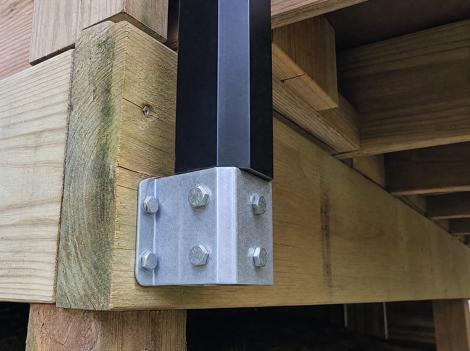 Close view of an aluminum guard post base bolted through a metal bracket into the rim joist and blocking of a deck frame with lag bolts