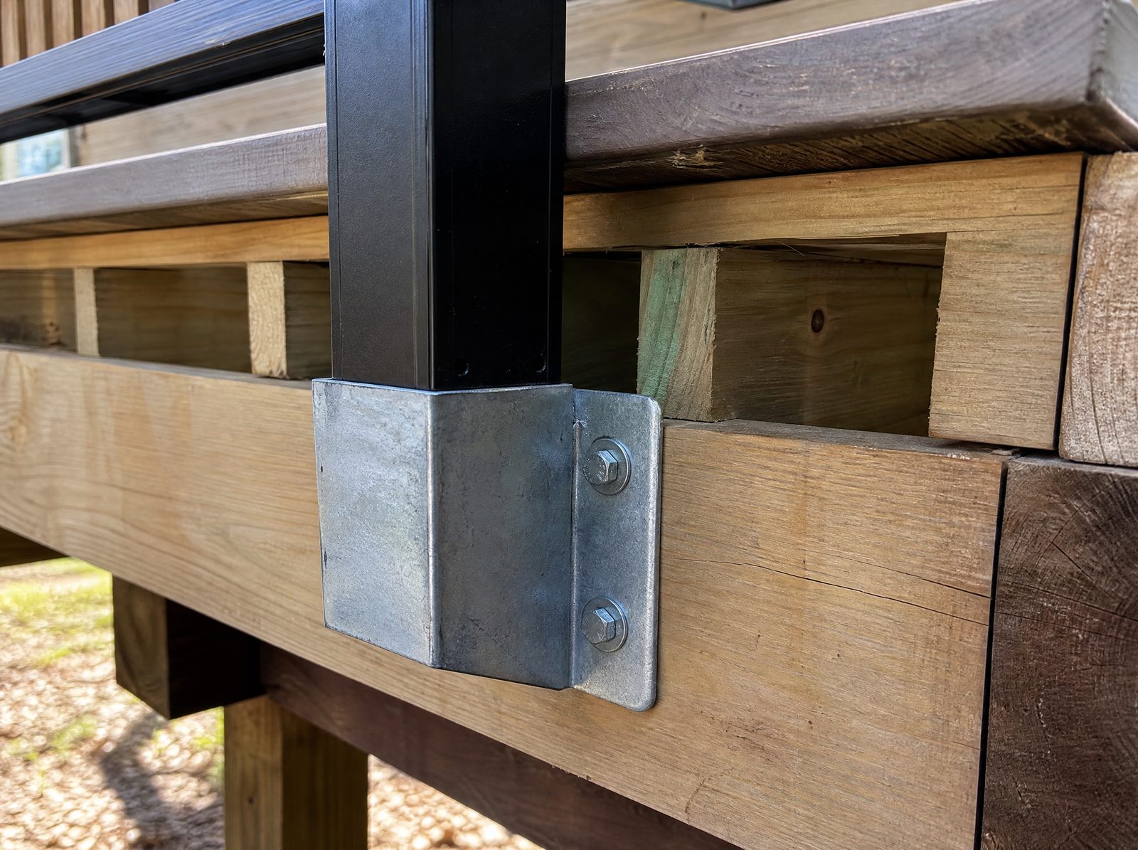 Black aluminum guard post base fastened to deck framing with a metal bracket and lag bolts driven into the rim joist and blocking