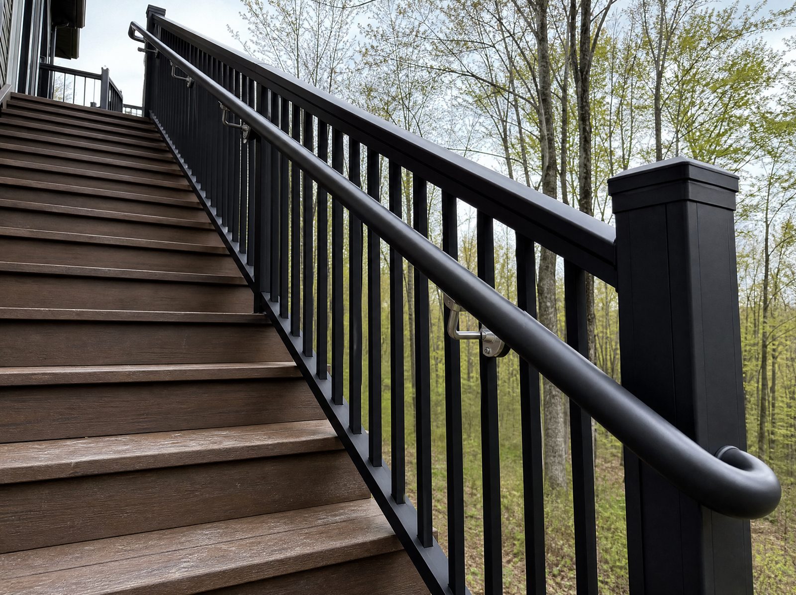 Round graspable metal handrail running down exterior stairs on brackets and returning cleanly to the post at the top and bottom of the flight