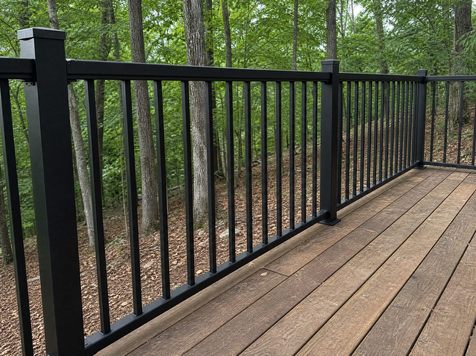 Black powder coated aluminum deck guard about thirty six inches high along the edge of a raised deck overlooking a wooded sloping backyard