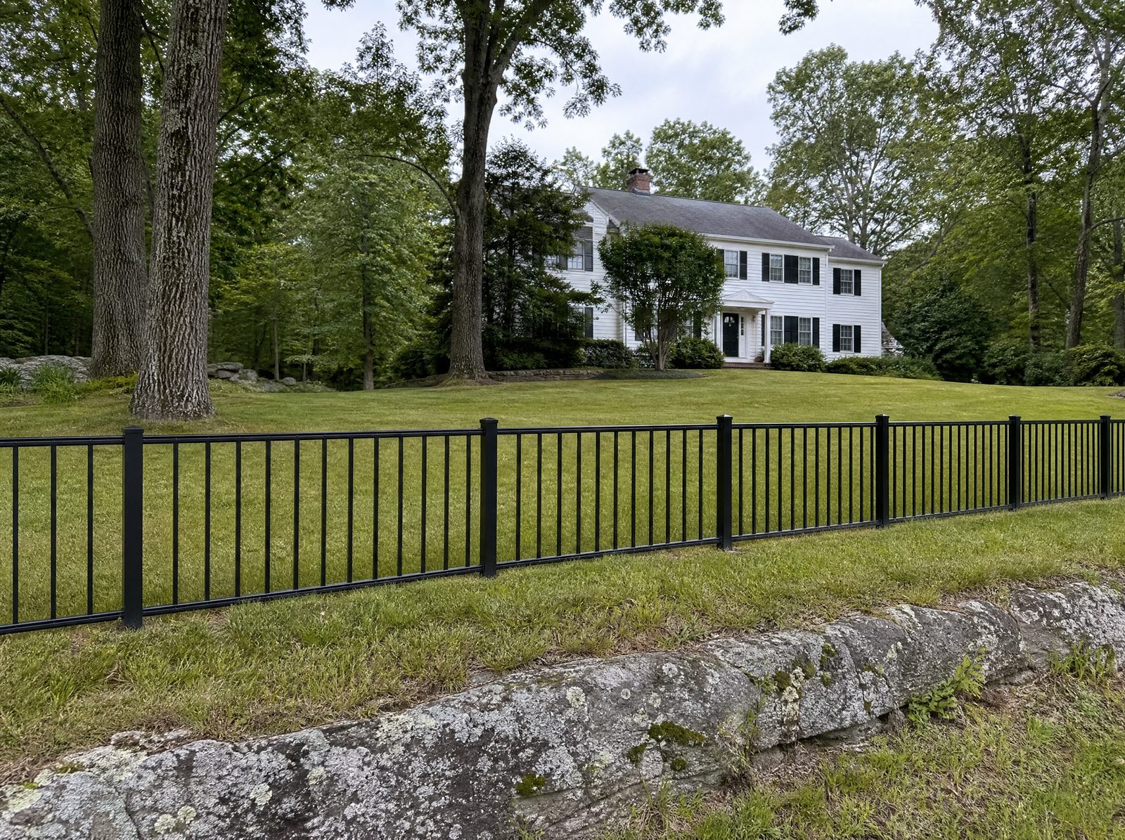 Low three foot open black aluminum fence marking the front property line of a New Fairfield colonial, an open see-through boundary rather than a privacy wall, with the house set well back