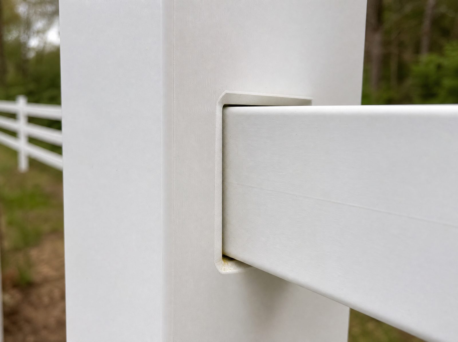 Close detail of a white vinyl rail meeting a white vinyl post at the routed rail pocket on a finished fence run, showing the thickness of the extruded profile and the satin surface of the PVC