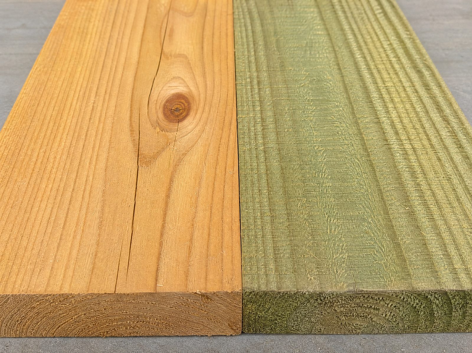 Close view of a warm cedar fence board face with grain and a tight knot laid beside a greener pressure-treated board so the two woods read as different materials