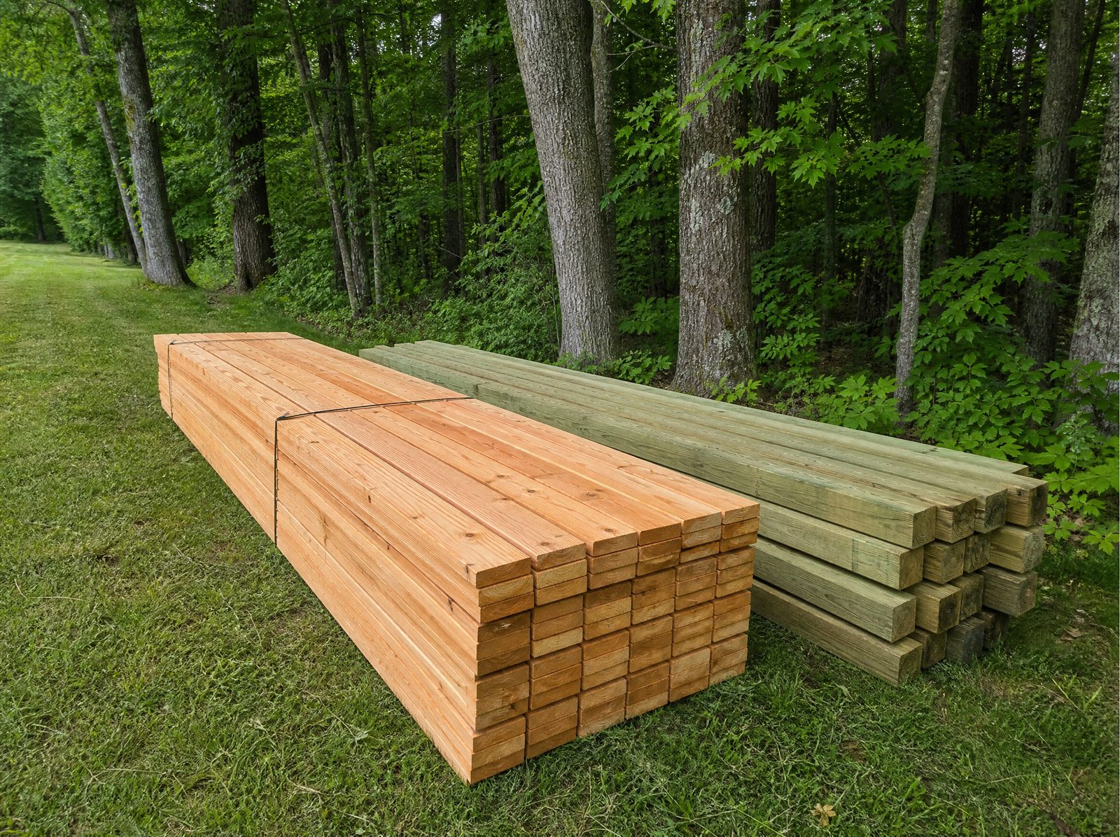 Cedar fence boards and pressure treated posts staged and stacked tidily along a wooded rural Sherman property line before installation