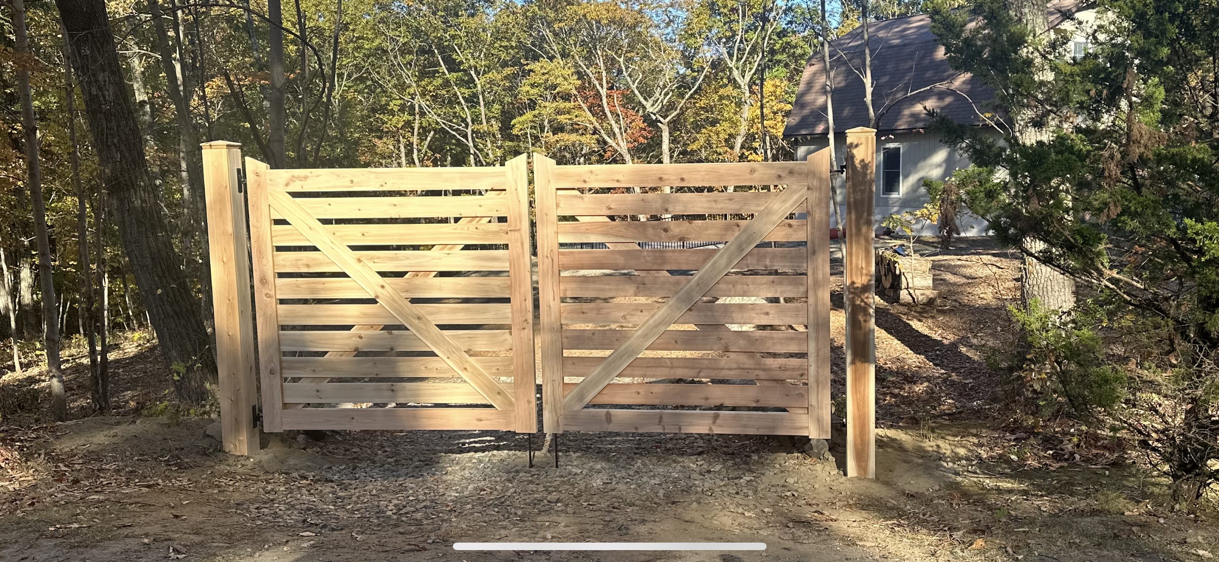 Wide horizontal-plank cedar double driveway gate with Z-brace backing set on a gravel drive in the woods