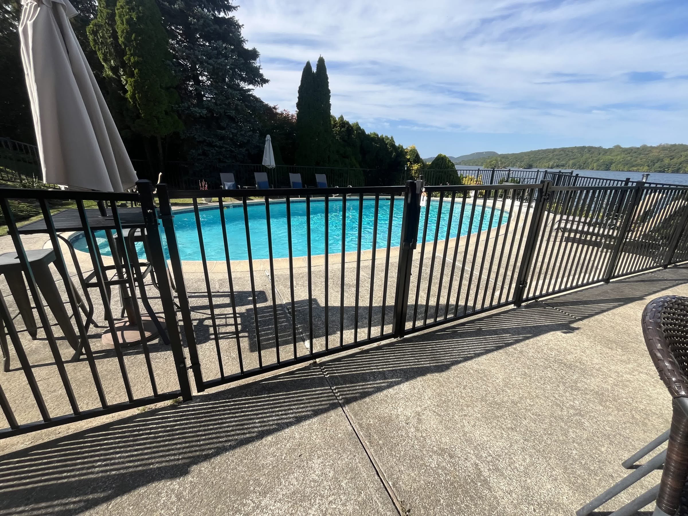 Black aluminum fence with a gate around an oval inground pool on a concrete deck with a lake and hills beyond