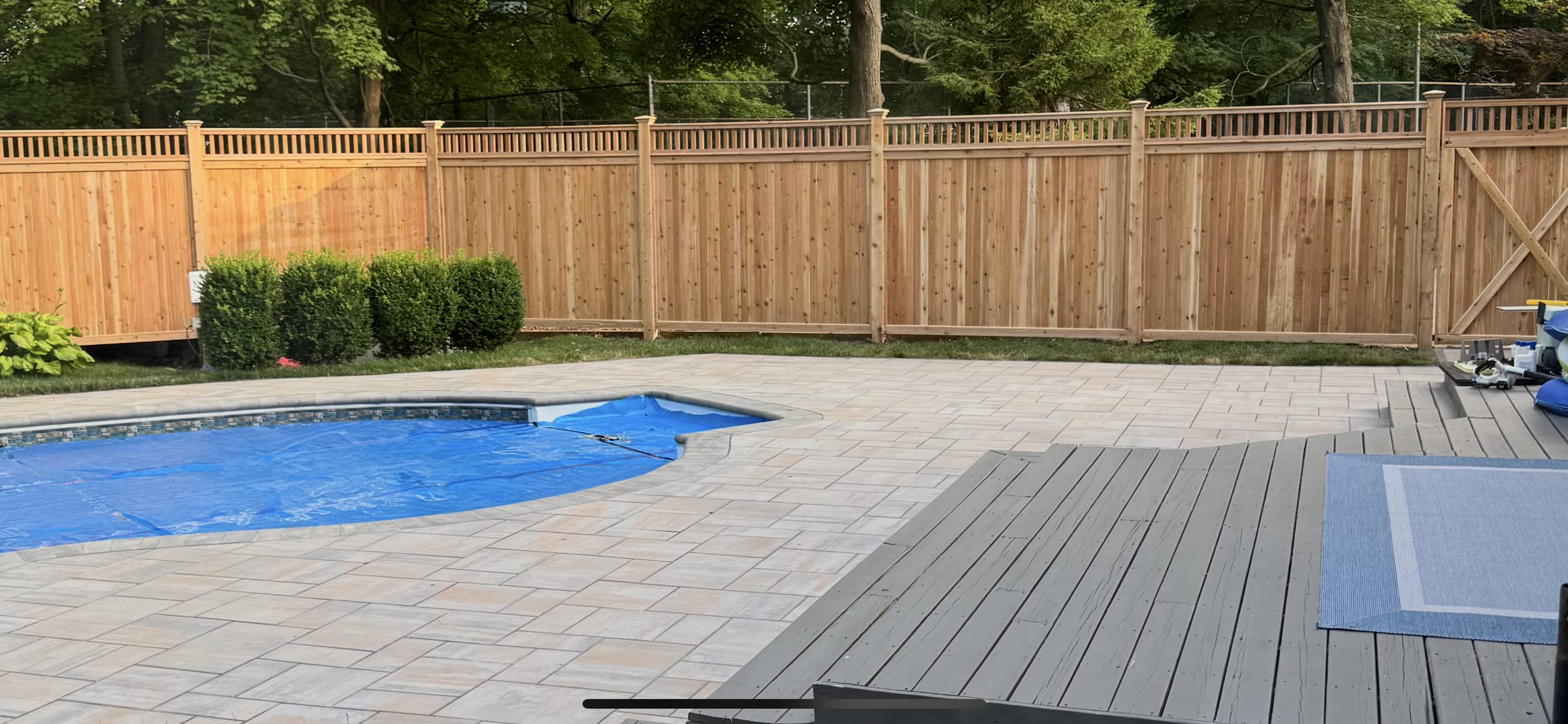 Cedar privacy fence with open spindle top section enclosing a paver pool deck and in-ground pool