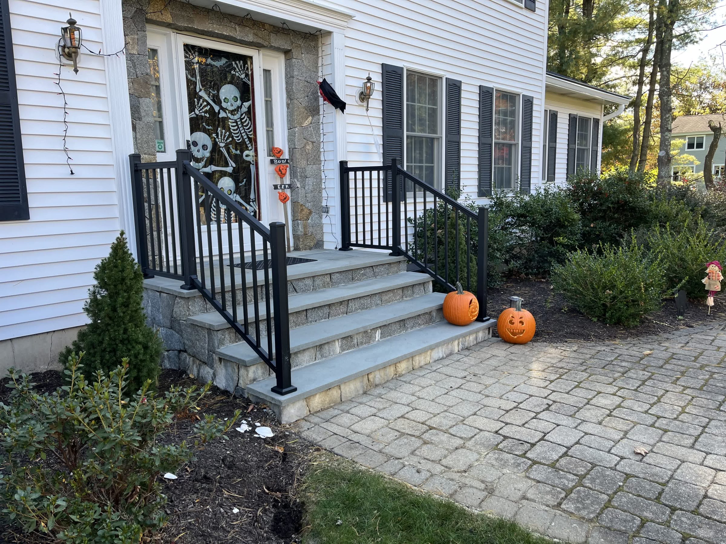 Black aluminum railings on stone entry steps of a white colonial home decorated with pumpkins for Halloween