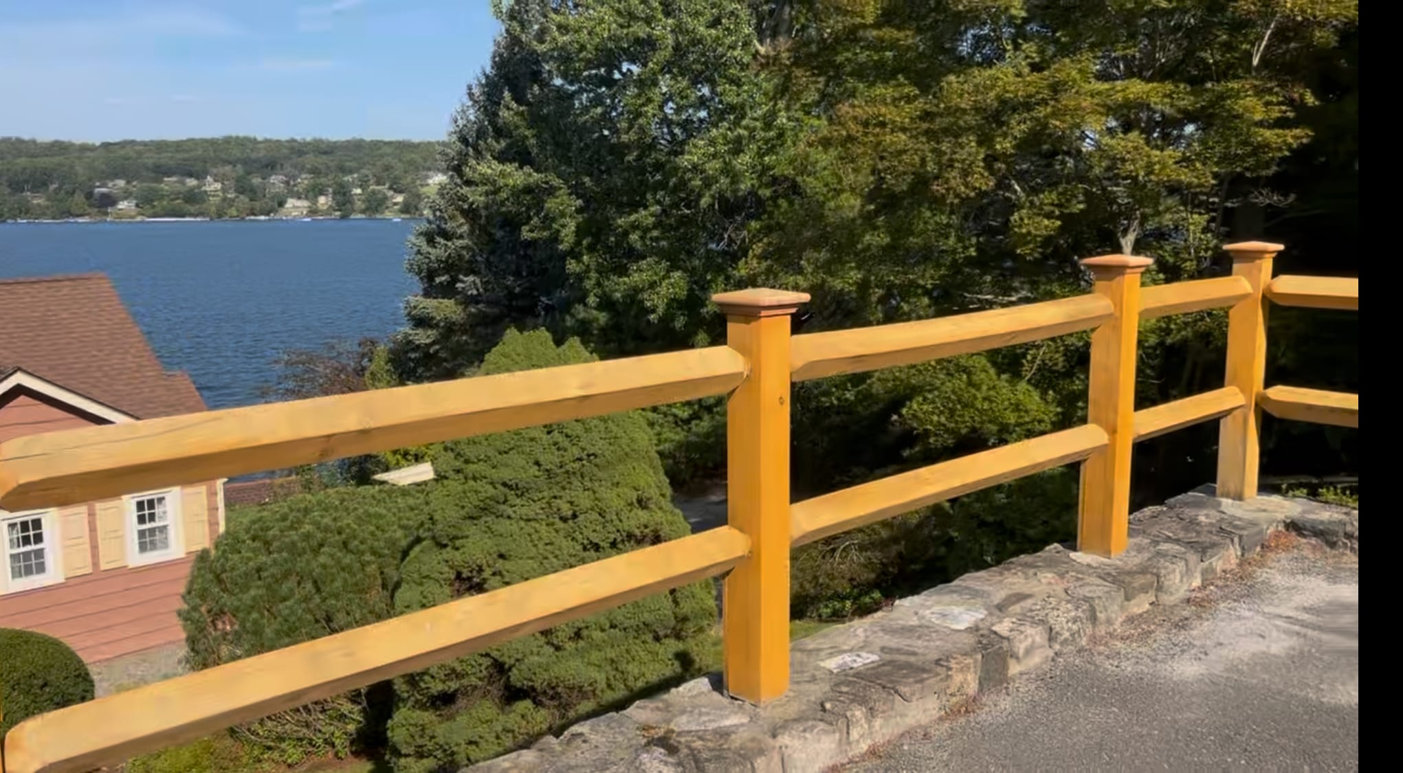 Honey-stained two-rail wood railing on a stone wall overlooking a lake and shoreline homes