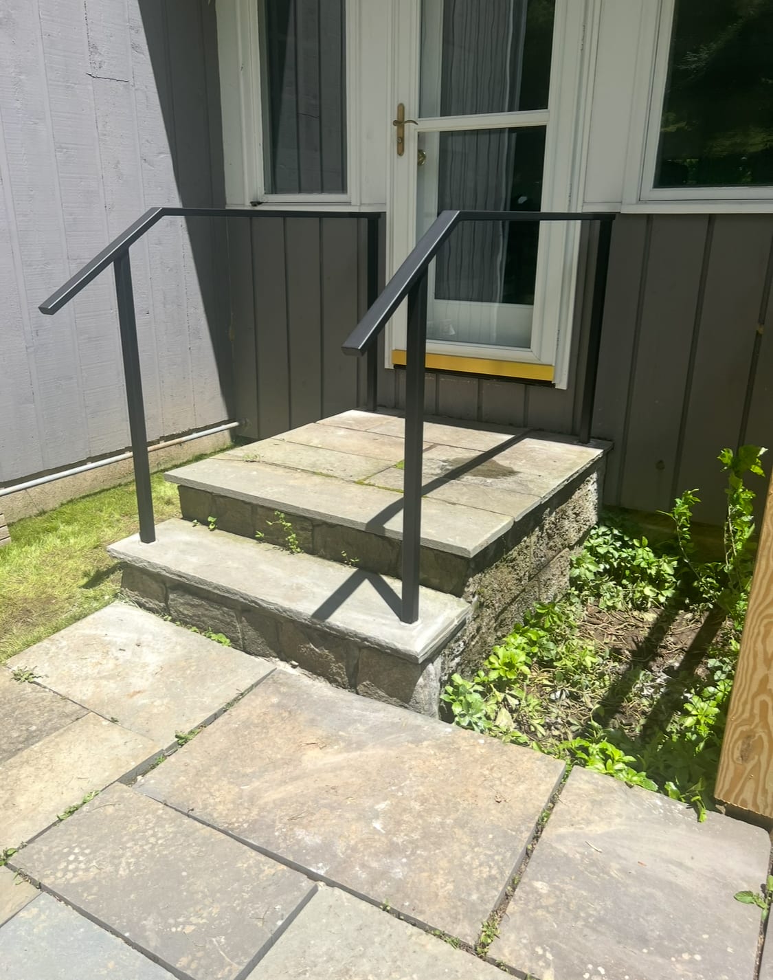 Pair of black metal handrails on a small bluestone stoop step against a gray board-and-batten house