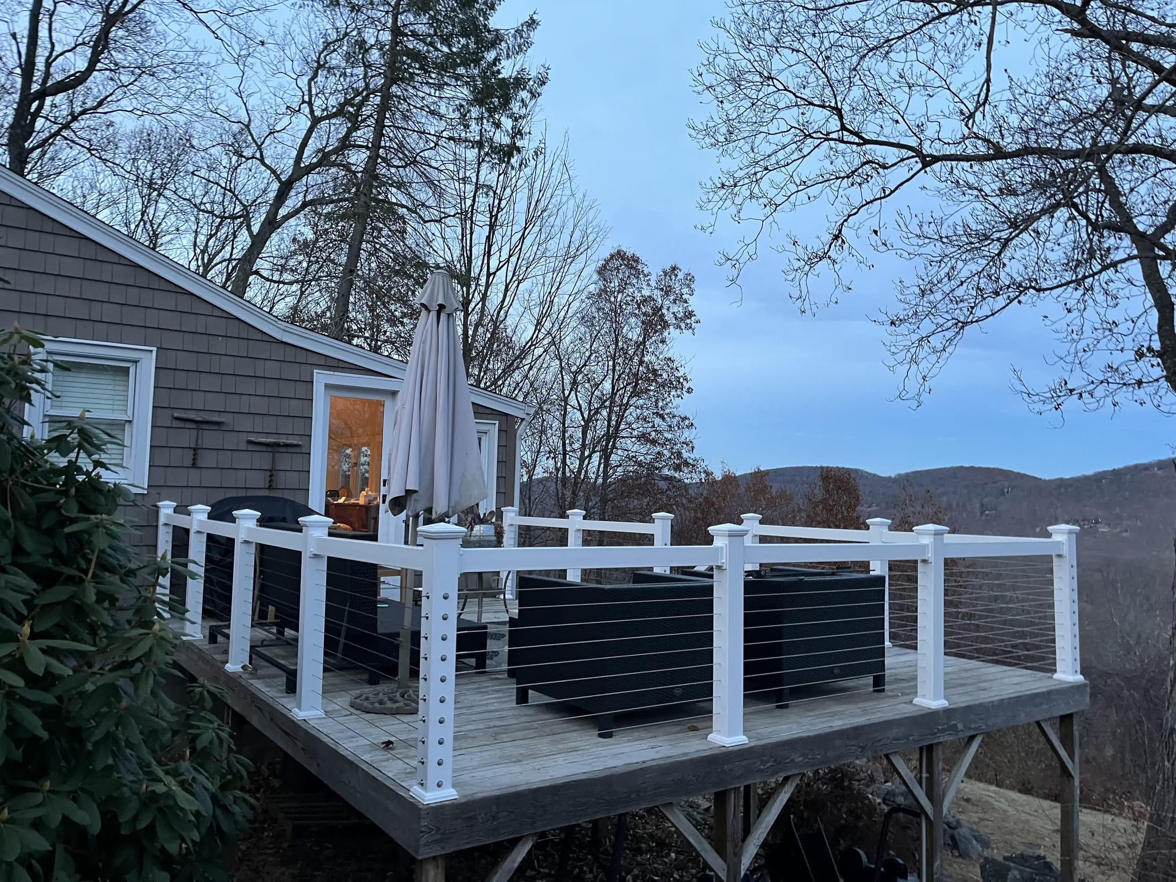 White vinyl posts with stainless cable railing around an elevated wood deck overlooking hills at dusk