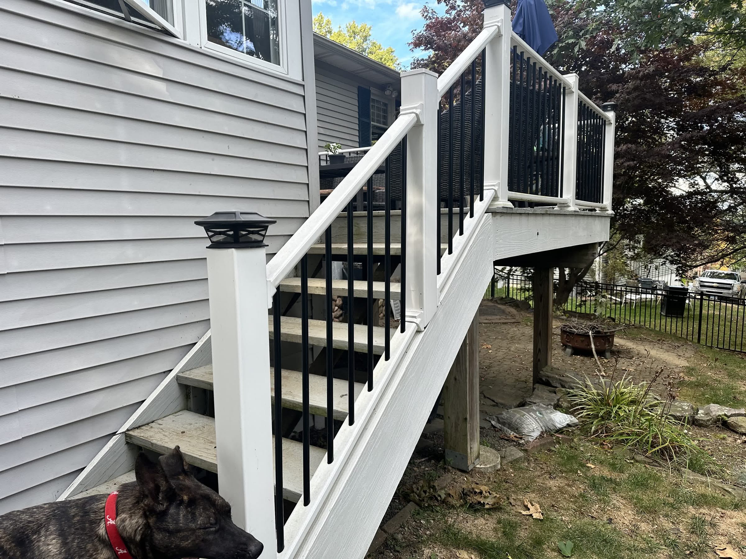 White vinyl posts and rails with black round balusters on wood deck stairs beside a gray house