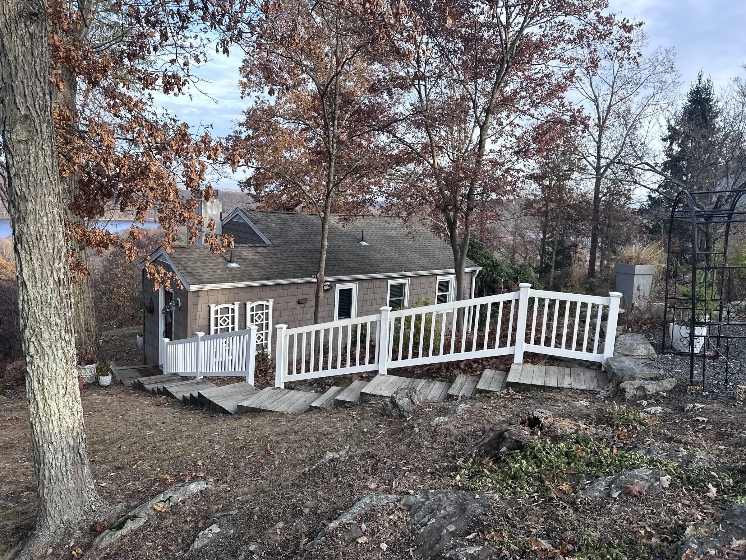 White vinyl railing along a wood ramp and steps leading to a shingled lakeside cottage among bare autumn trees