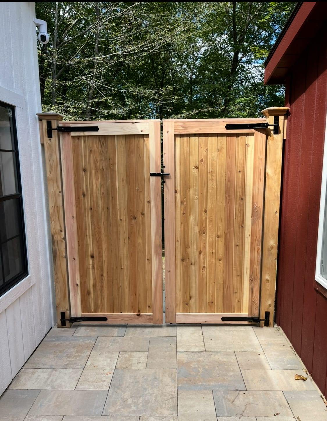 Natural cedar board double gate with black hardware set on a bluestone patio between a white and red building