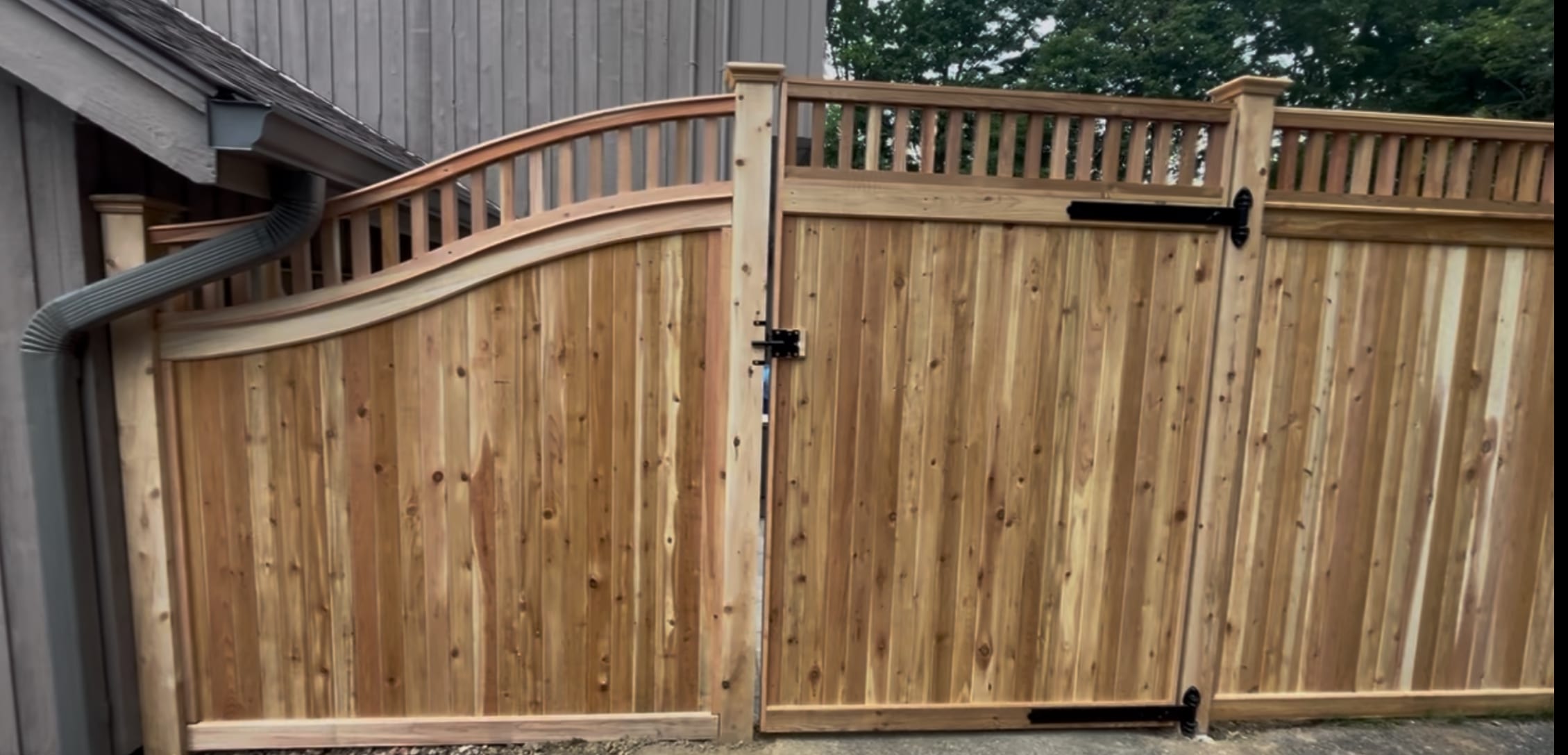 Cedar privacy fence with open spindle topper and an arched scalloped transition panel beside a gate