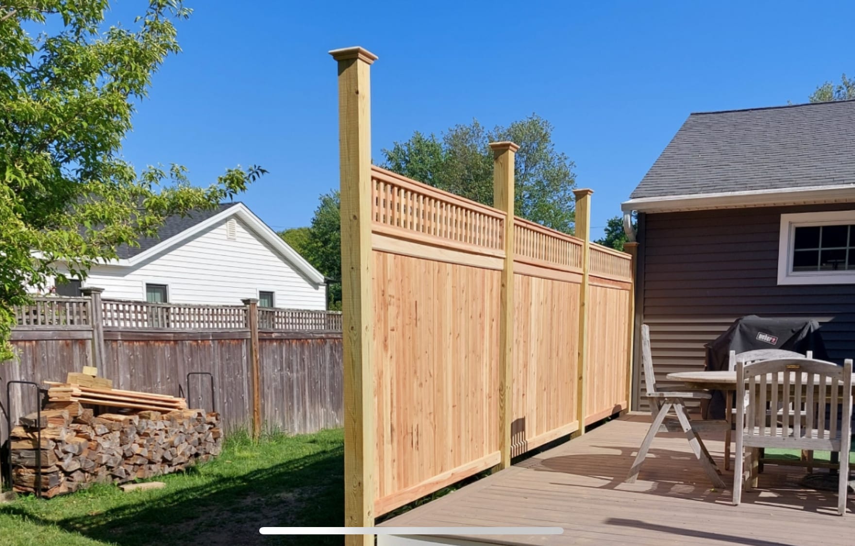 Cedar semi-private fence with paneled base and open spindle top mounted along a composite deck beside a house