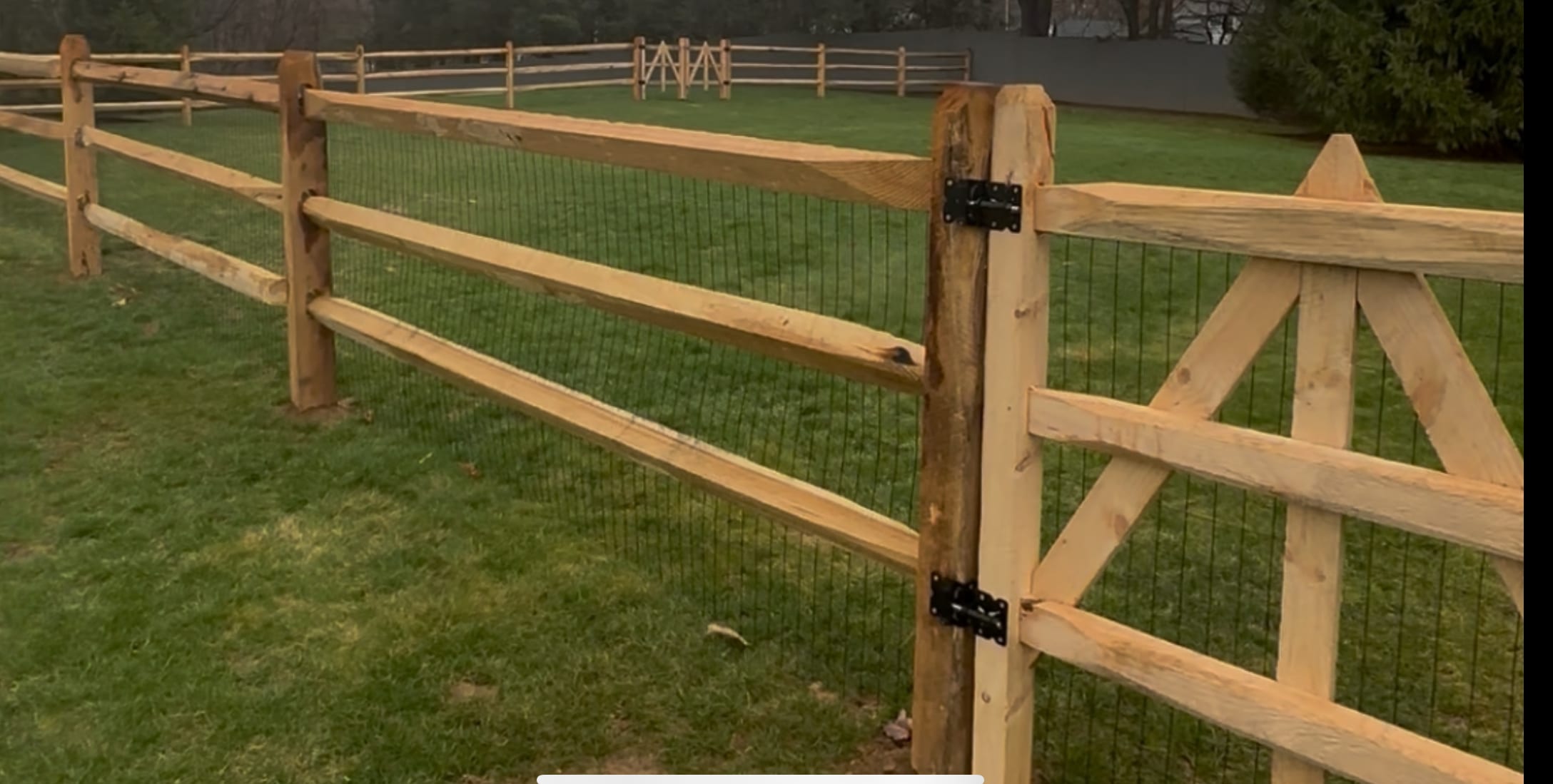 Three-rail cedar split-rail fence with black wire mesh and a matching swing gate around a lawn