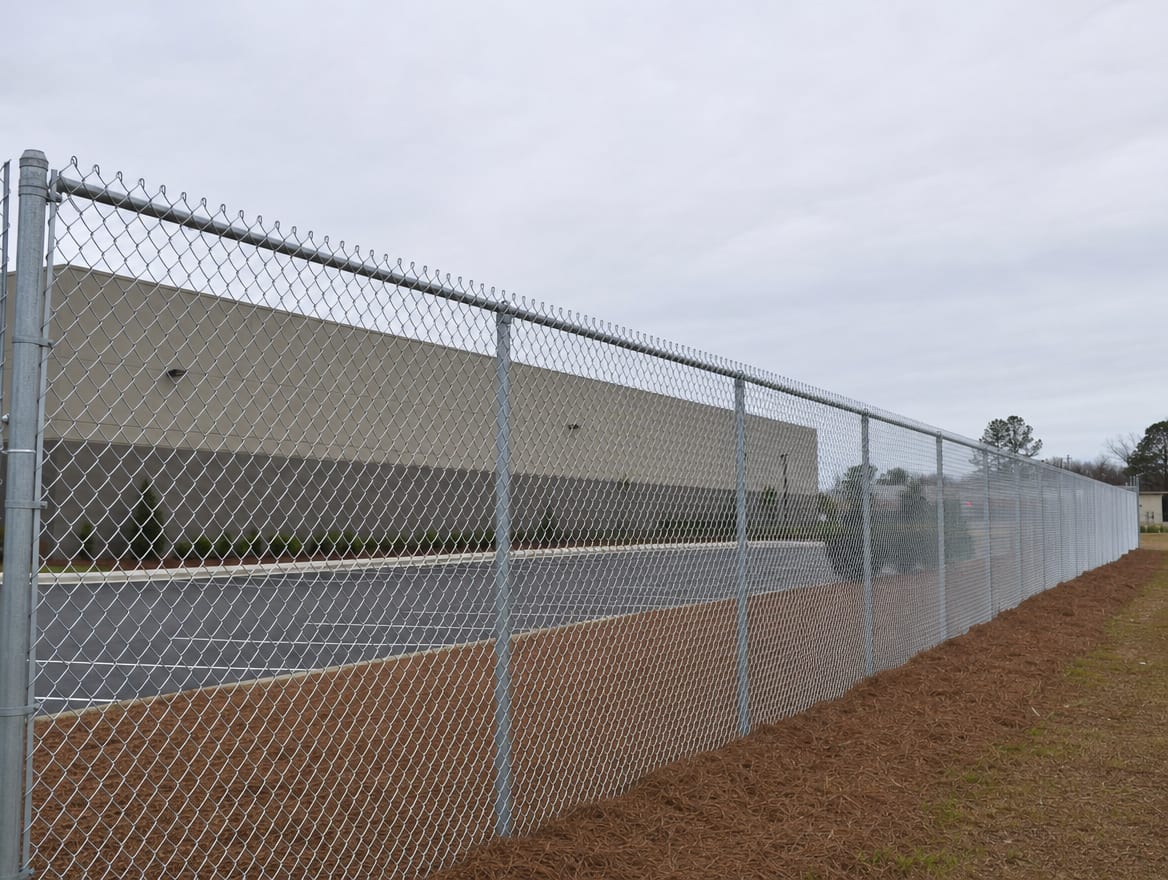 A chain link perimeter fence running alongside a warehouse building