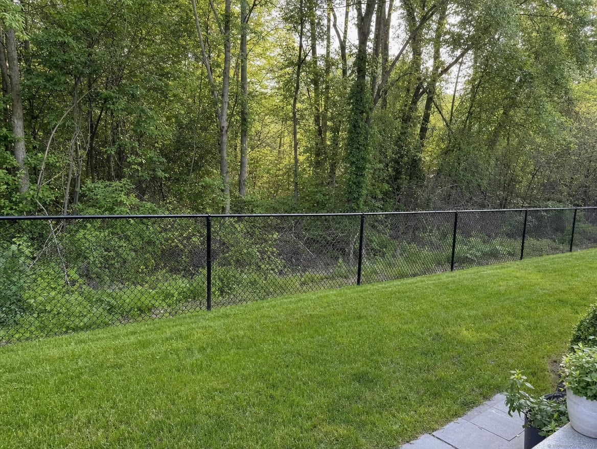 A black chain link fence running along the rear property line of a compact backyard in Fairfield, CT
