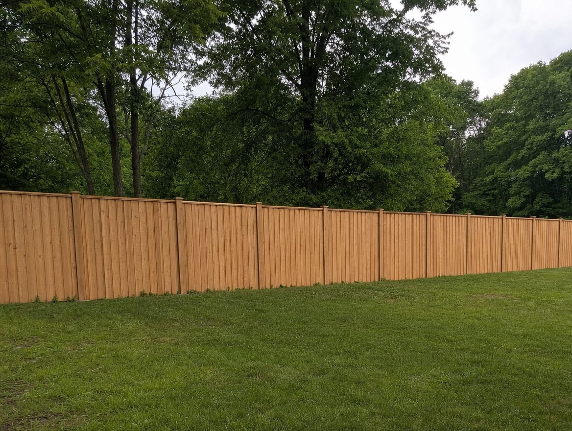 A full six foot tall wood privacy fence running along the back property line of a farmhouse yard in Goshen, CT