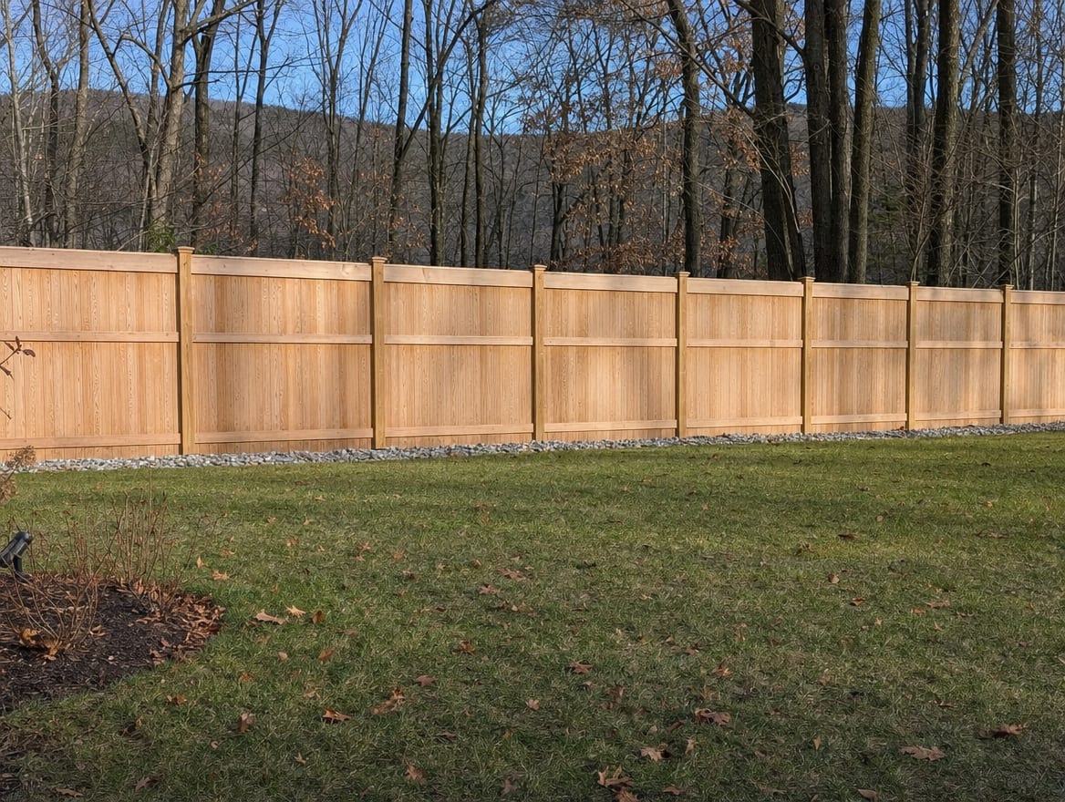 A full six foot tall wood privacy fence running along the back property line of a farmhouse yard in Kent, CT