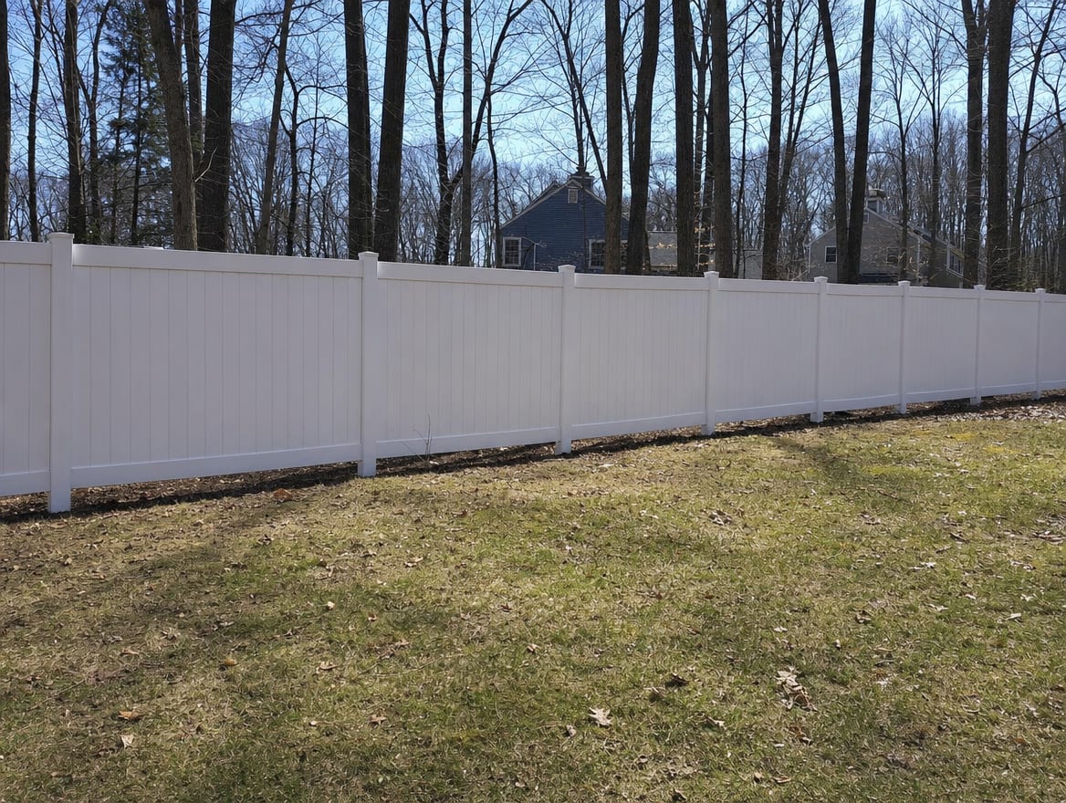 A full six foot tall white vinyl privacy fence running along a backyard property line in Meriden, CT