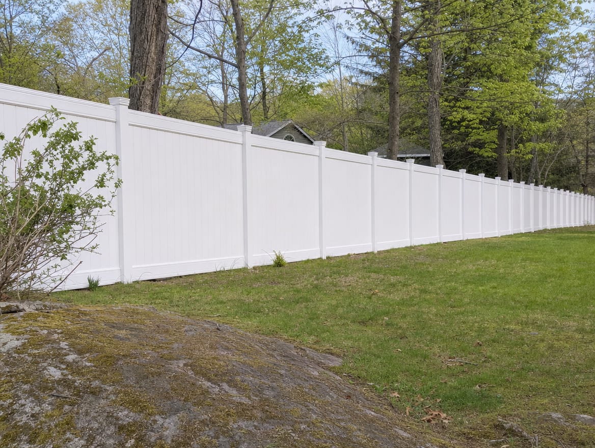 A full six foot tall white vinyl privacy fence running along a backyard property line in Pound Ridge, NY