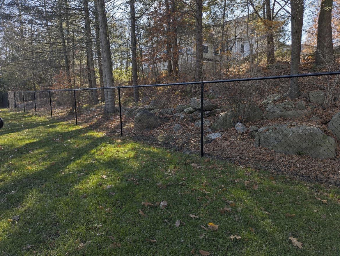 A black chain link fence running along a rear property line of a backyard in Pound Ridge, NY