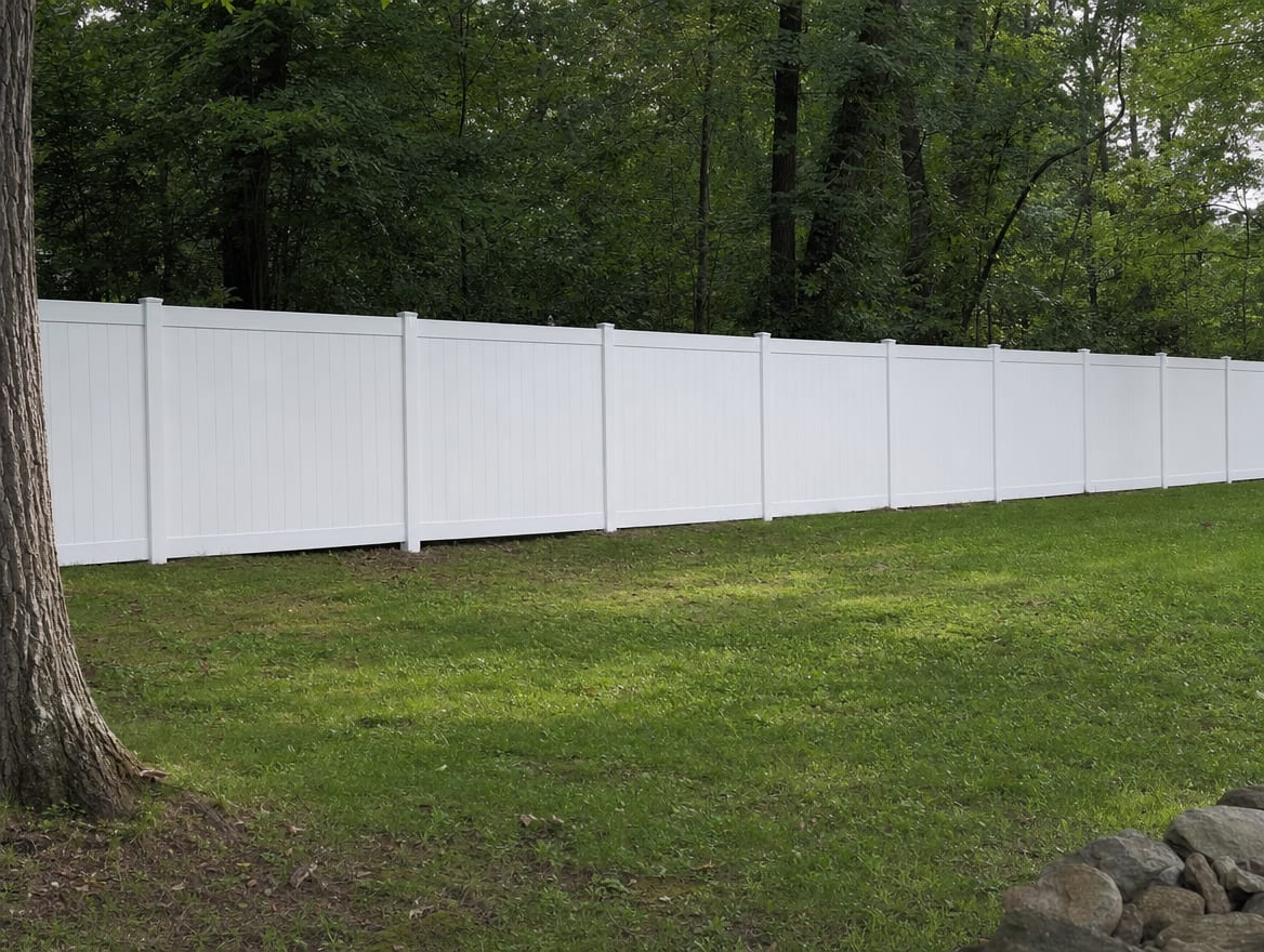 A full six foot tall white vinyl privacy fence running along a backyard property line in Thomaston, CT