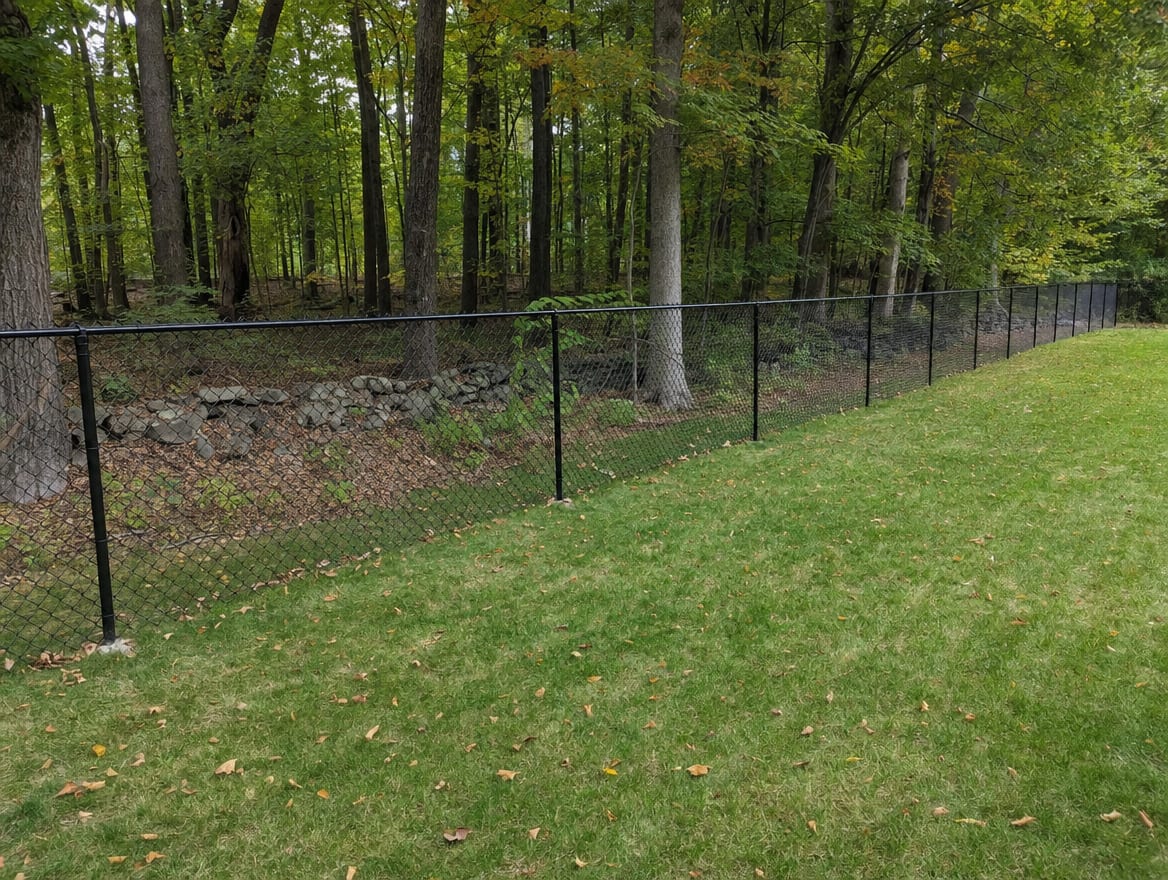 A black chain link fence running along a rear property line of a backyard in Watertown, CT