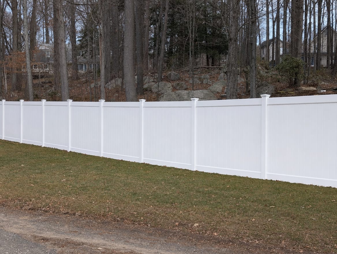 A full six foot tall white vinyl privacy fence running along a backyard property line in Weston, CT