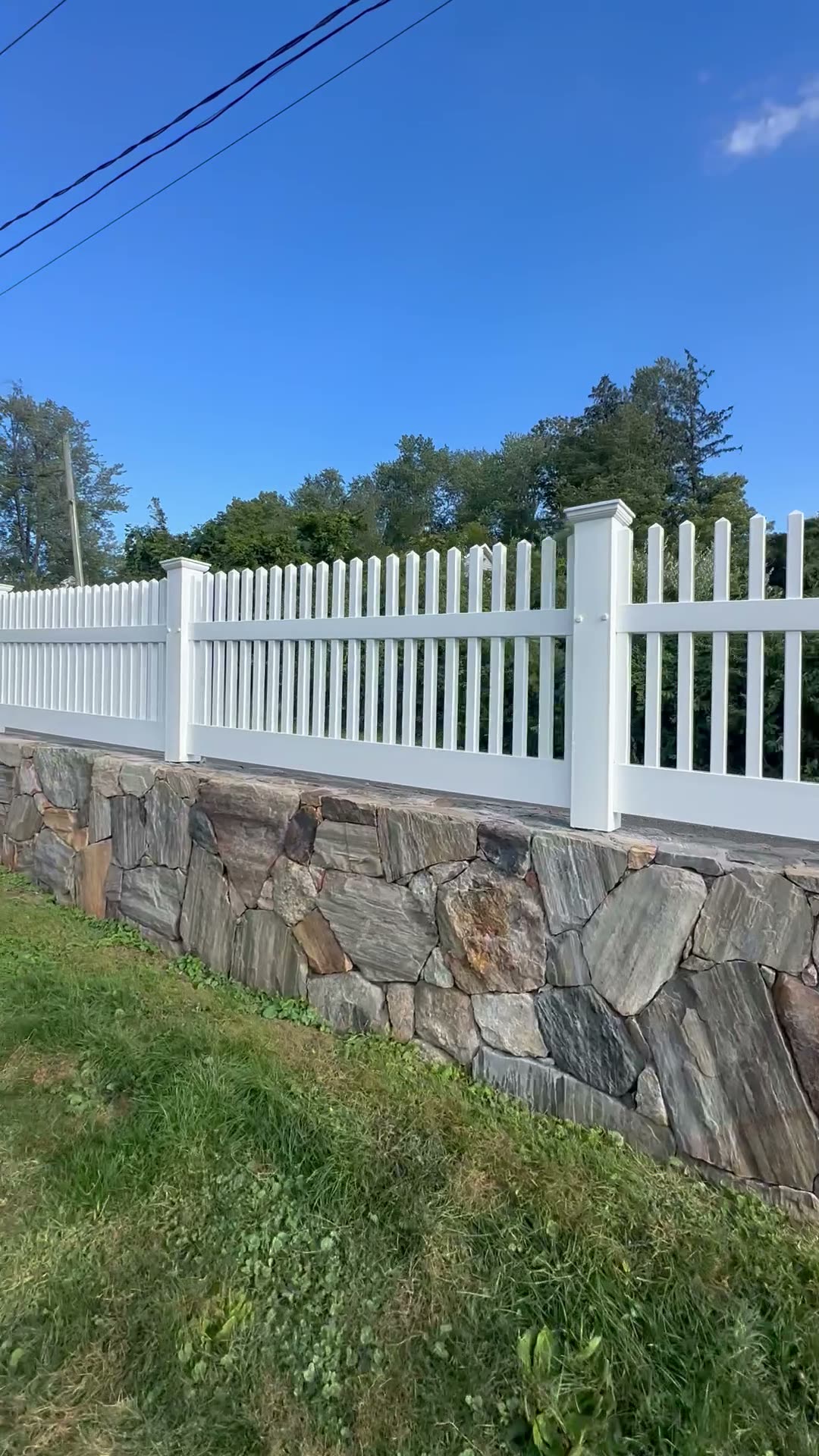 White vinyl picket fence set atop a fieldstone retaining wall
