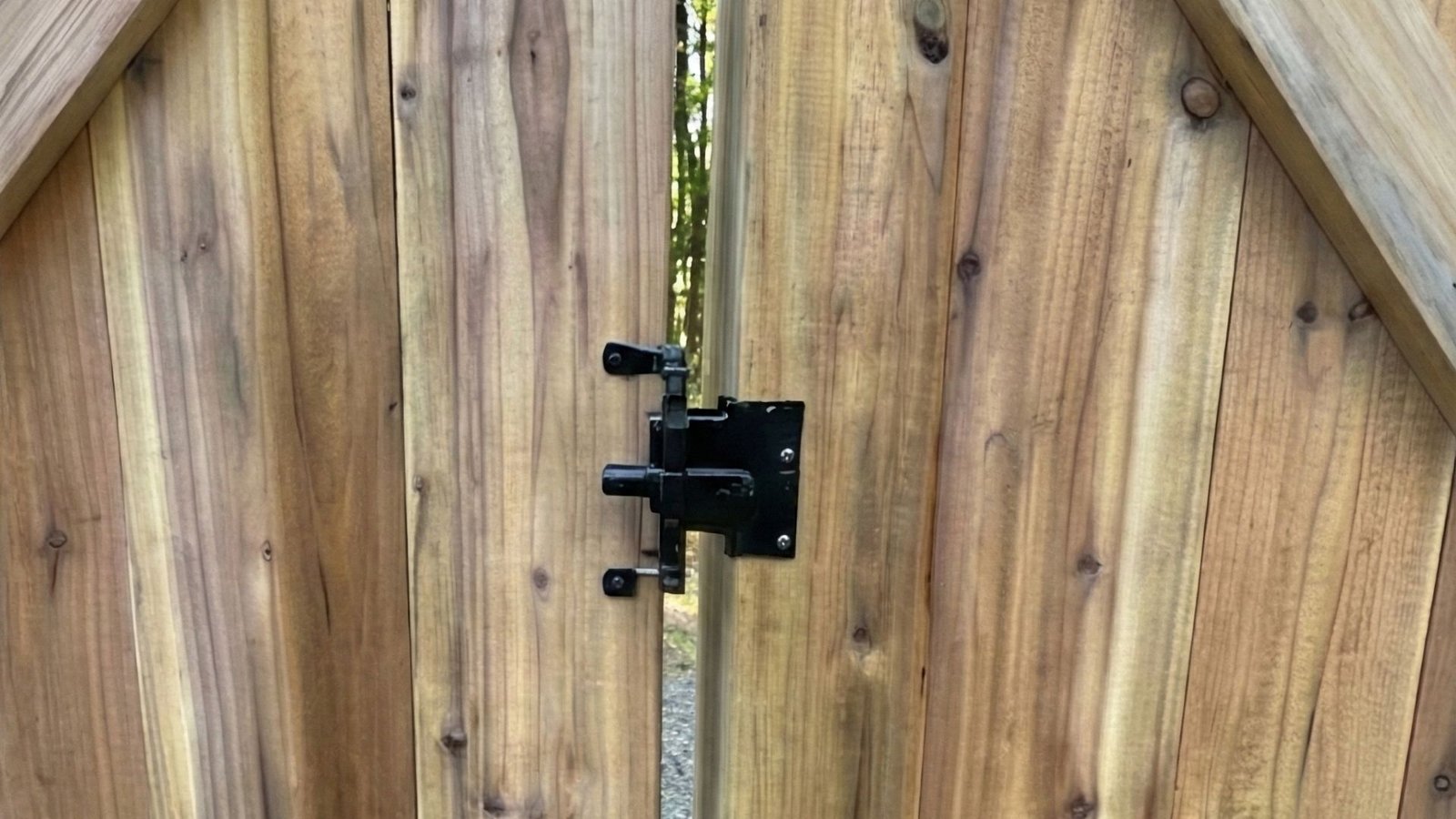 Black metal gate latch hardware installed on natural wood fence gate with vertical cedar planks