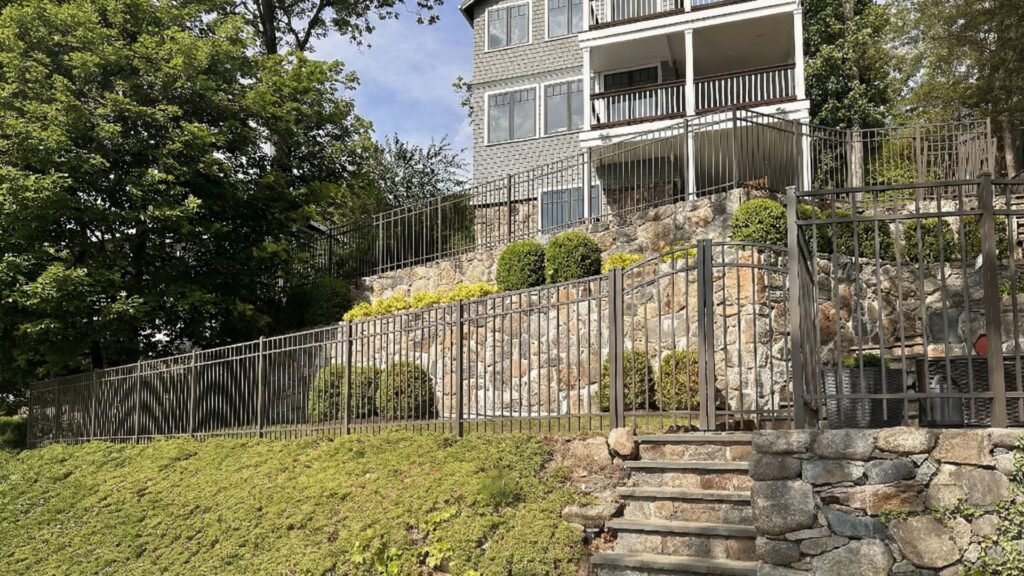 Two-story house with aluminum fencing along stone retaining wall and metal railings on deck balconies