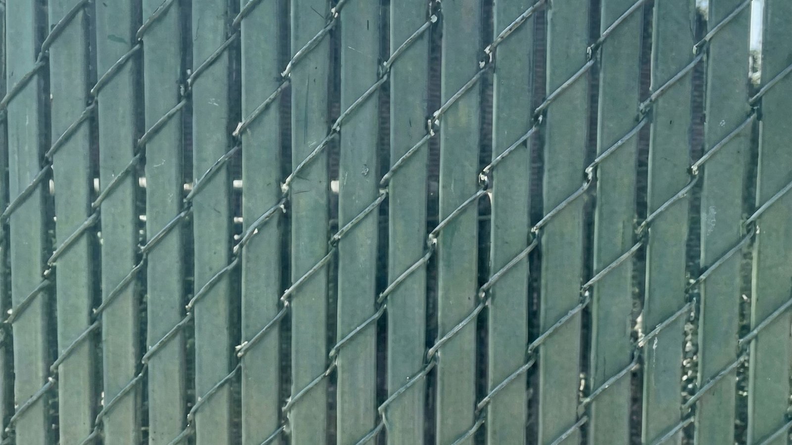 Close-up view of green privacy slats woven through chain link fence creating solid barrier