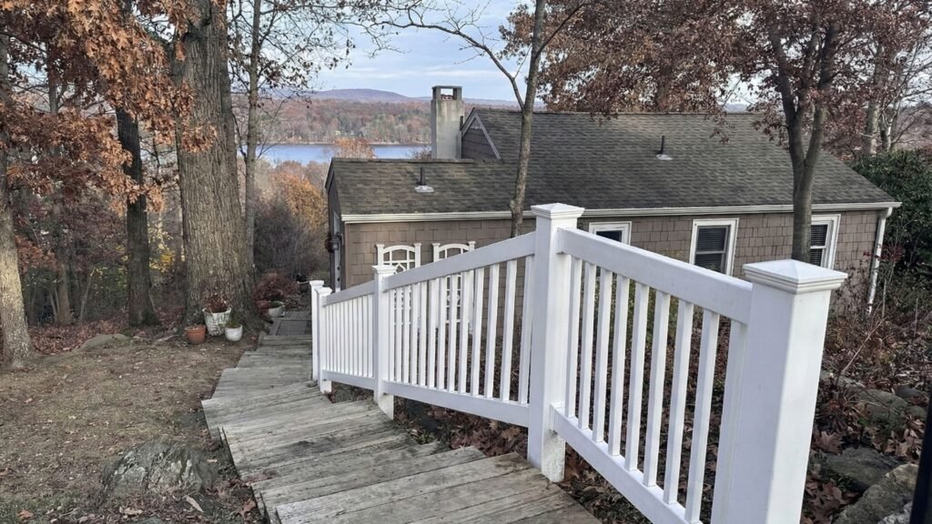 White wooden deck railing with vertical balusters overlooking lake and autumn foliage in residential backyard